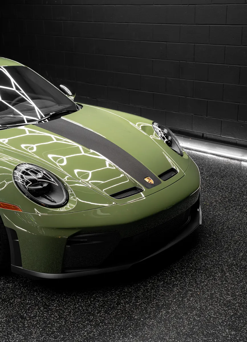 Front of an olive green Porsche 911 GT3 showing the nose, headlight and hood stripe
