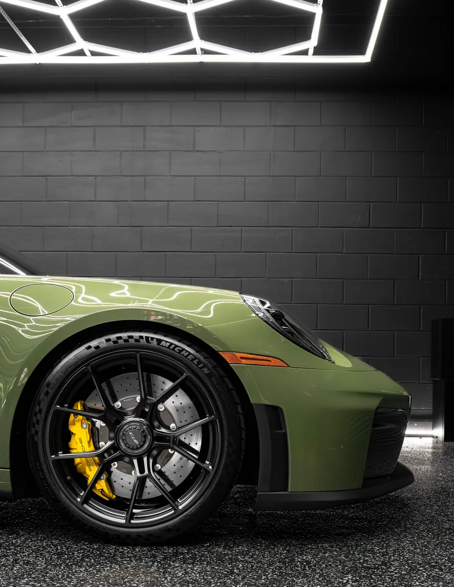 Front wheel and fender of an olive green Porsche 911 GT3 with yellow brake calipers