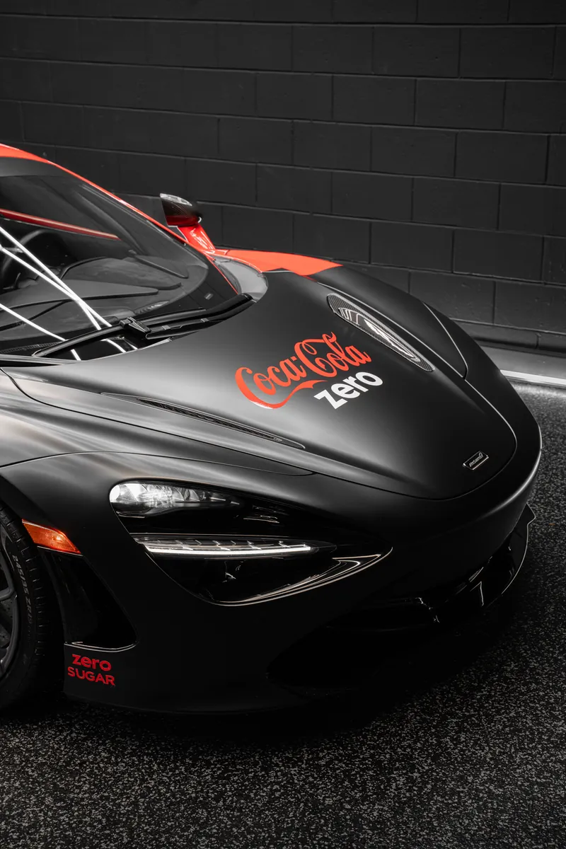 Front of a McLaren 720S with a matte black and red custom livery wrap and Coke Zero logo on the hood