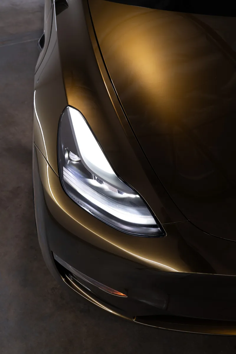 Headlight and hood of a bronze Tesla Model Y